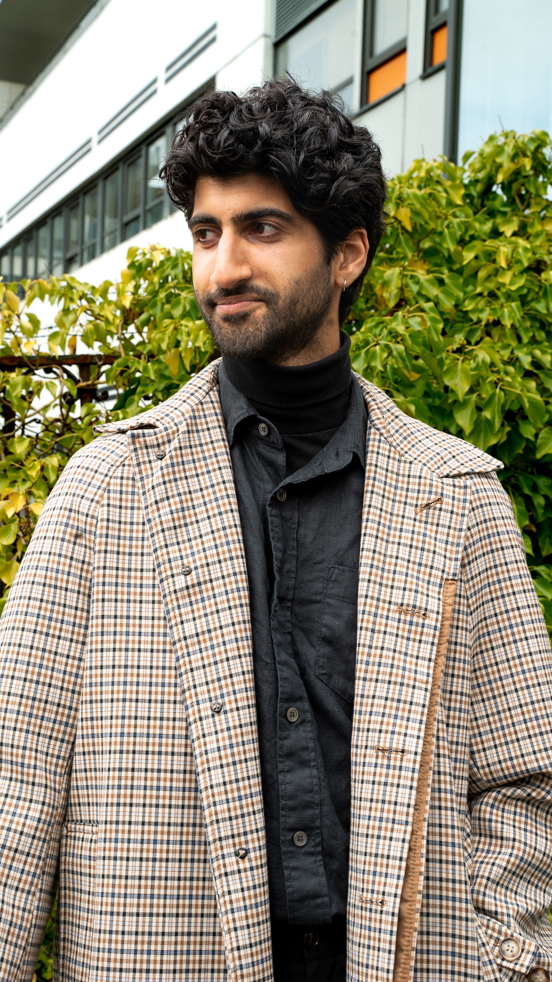 Karan står foran en grønn busk og smiler lurt mens han ser til venstre