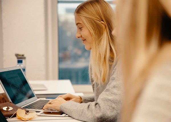 Jente med blondt hår som skriver på datamaskinen mens hun smiler. 