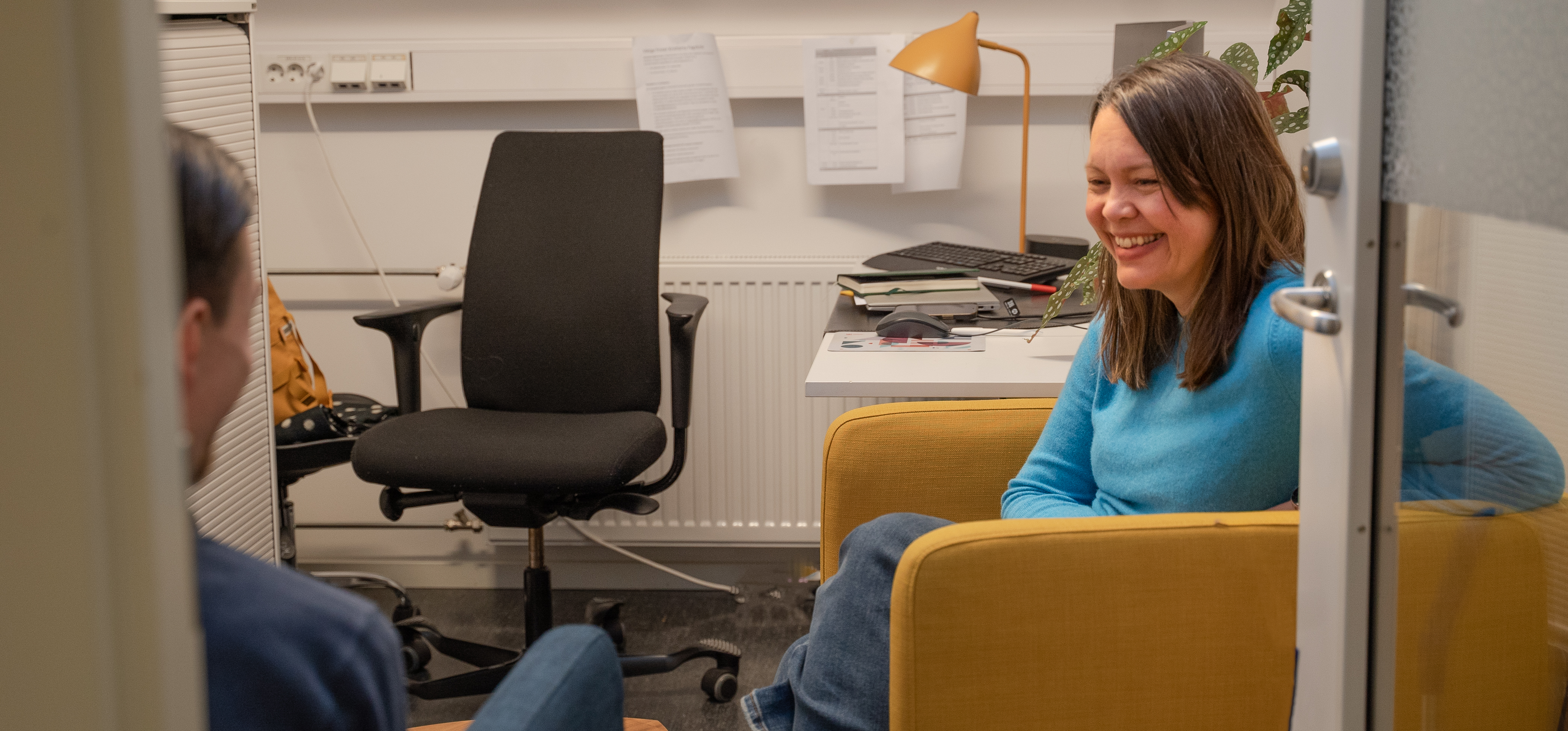 Tone sitter og smiler på kontoret sitt og snakker med en student.