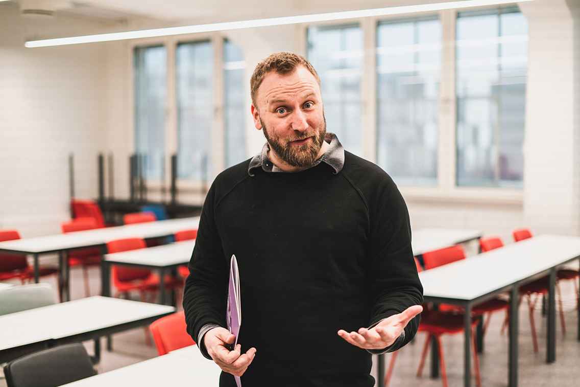 Kai Schwind på Ar@k 2019 står og gestikulerer med et program i den ene hånden i et klasserom