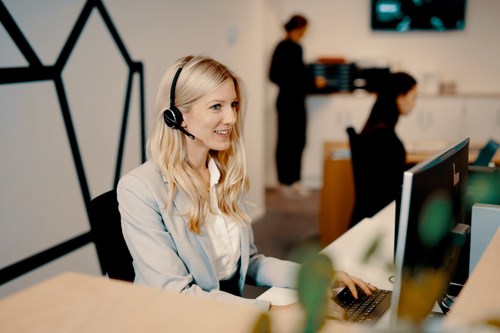 Foto av en kvinne som sitter med øretelefoner foran en skjerm og har samtale med student.