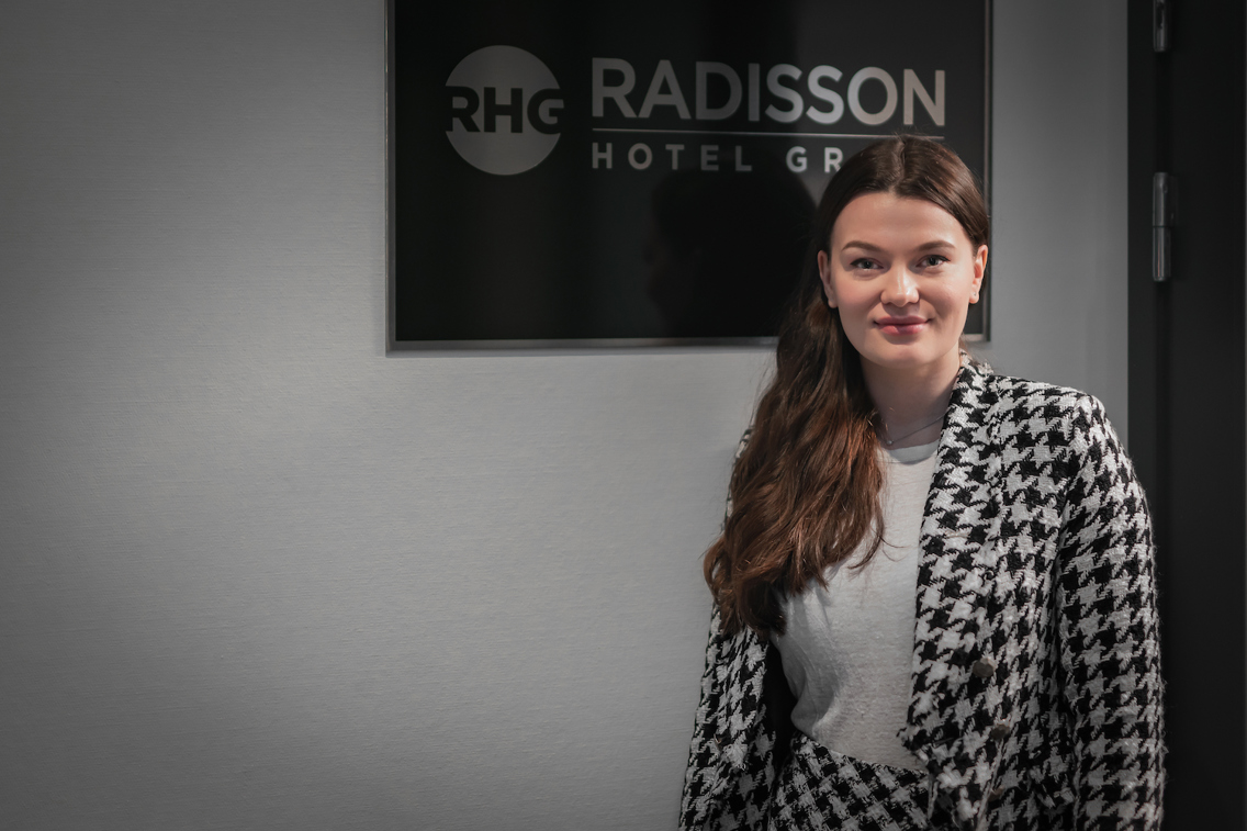 Foto av kvinne foran et Radisson Hotel Group-skilt.