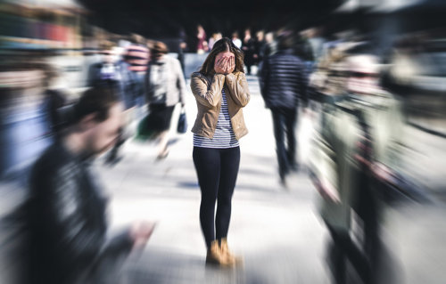 Woman standing with her hands covering her face while everybody else is moving quickly around her