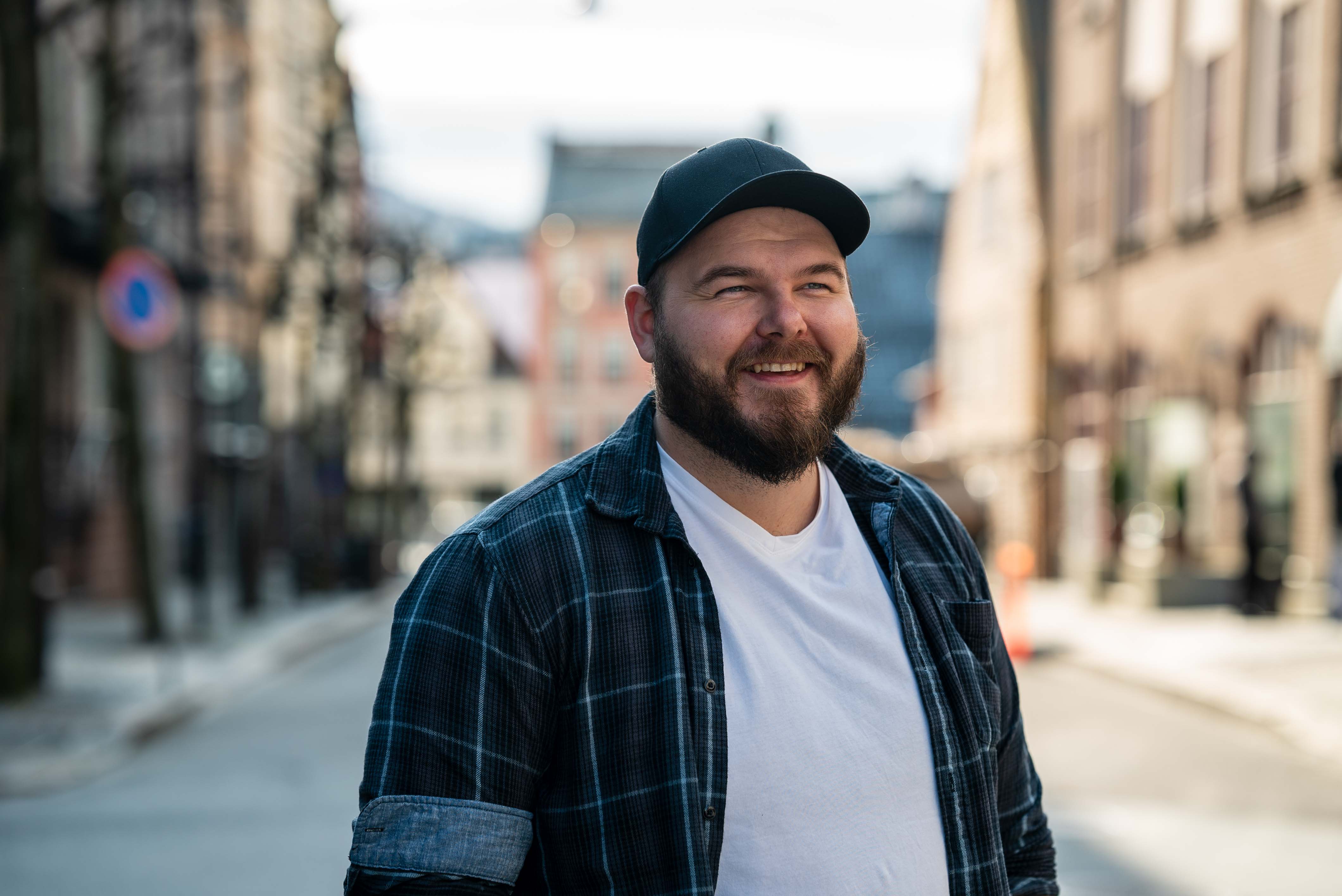 Foto av en smilende mann med caps midt i Bergens gater.