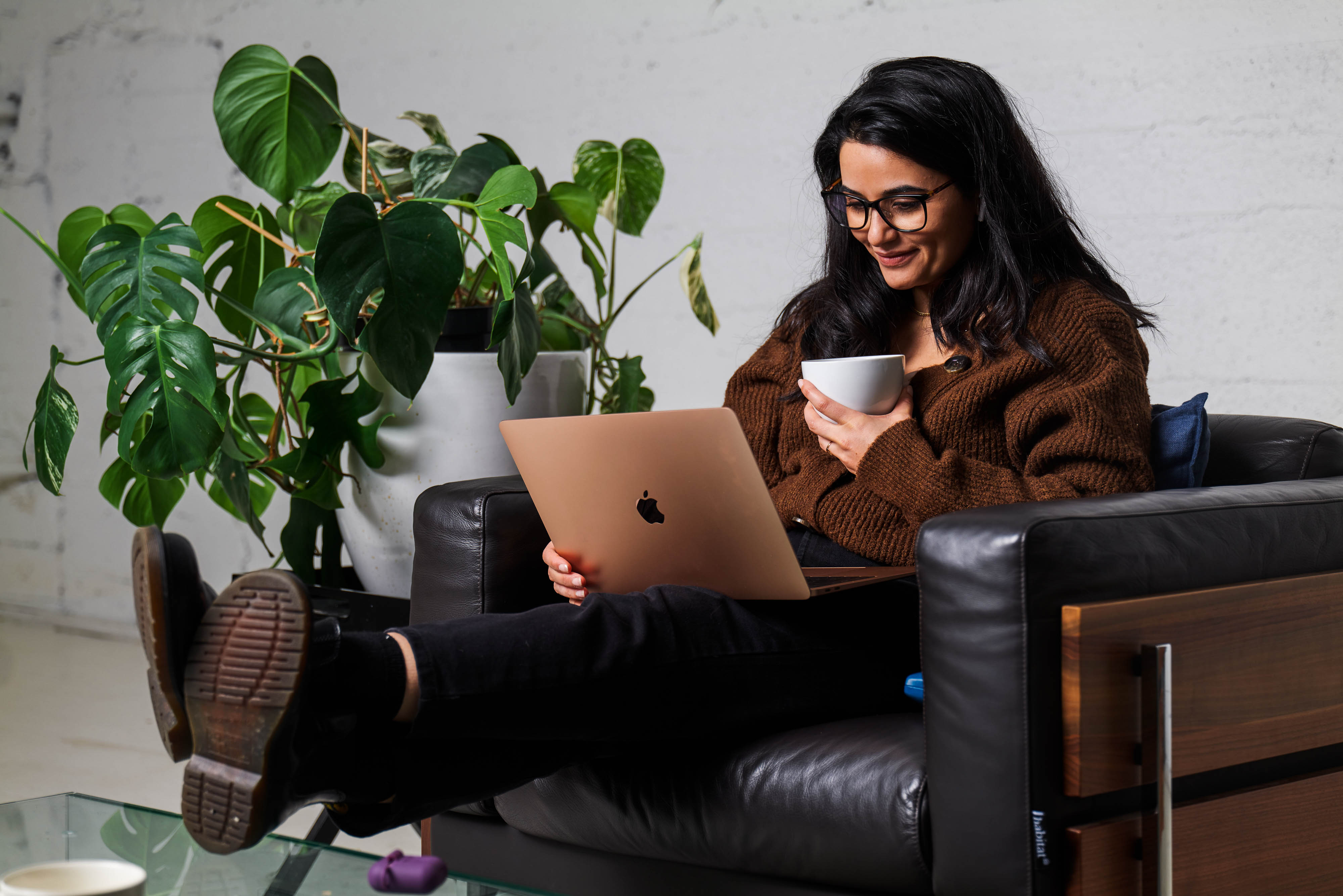 Ung dame med mørkt hår og briller sitter med beina høyt og med laptop på fanget.