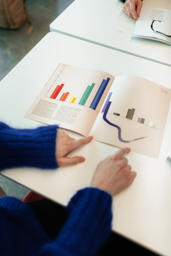 Foto av hender som peker på grafer i en bok.