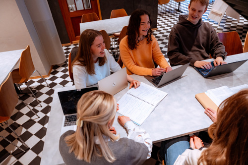 Fire studenter sitter rundt et bord og ler.