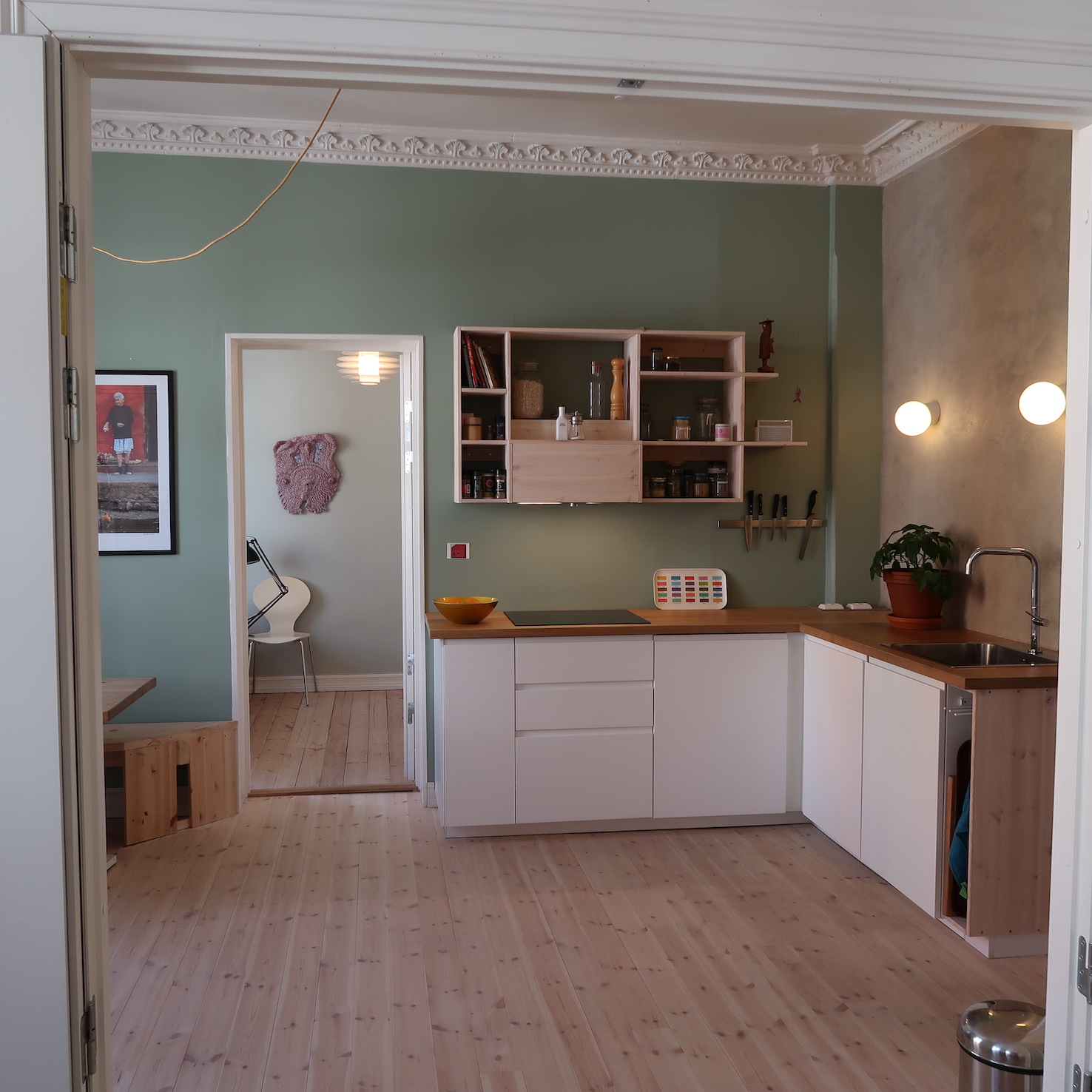 Bilde av kjøkken hvor man ser inn til soverommet. I hjørnet står kjøkkenbenk og vask, rommet har få ting og er åpent. En vegg har upusset mur, mens de andre er malt.