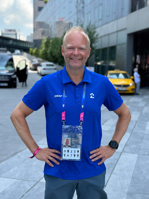 Vegard Jansen Hagen ser opplagt inn i kamera og smiler. Han har blå Craft-tskjorte med TV2-logo på, og et akkrediteringsbevis hengende rundt halsen.
