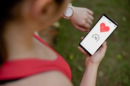 Dame som ser ned på telefonen som er koblet til en treningsklokke og viser hjerterytmen.