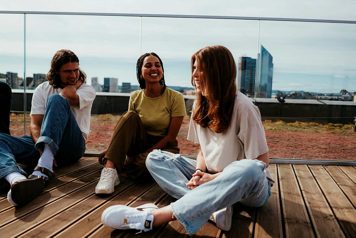 Foto av tre studenter som sitter på en gangbro.