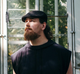Bilde av mann med skjegg og sixpence som poserer foran et vindu.