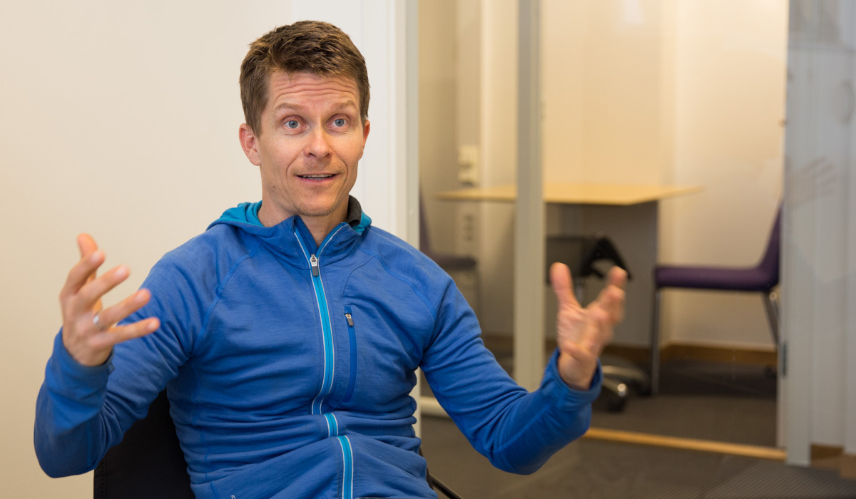 Ole Petter Hjelle sitter inne på et rom og forklarer engasjerende med armene under et intervju.