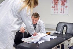 Foto av mannlig og kvinnelig student i hvite frakker som studerer en bok.