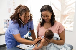 A doctor is listening to the heart of a baby who is being held by mother