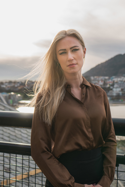 Portrettfoto av kvinne på en takterrasse, i bakgrunnen ser man en by ved vannet.