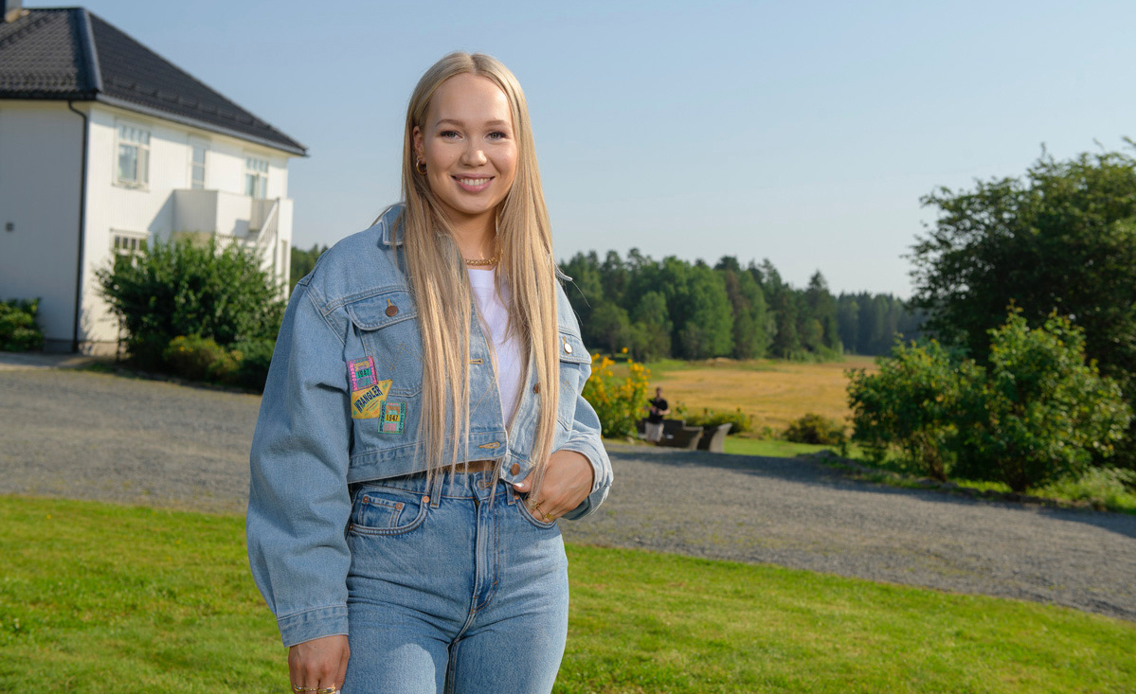 Bilde av Agnete Saba hvor hun smiler. Hun har langt blondt hår og er kledd i dongeri fra topp til tå.
