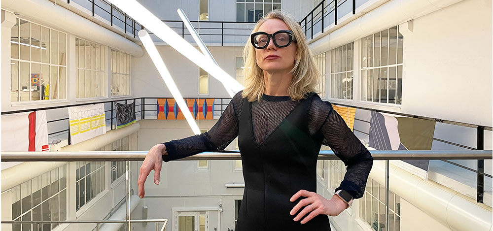 Professor Vesmá Kontere McQuillan poserer for kamera i sort kjole og briller inne på Høyskolen Kristiania