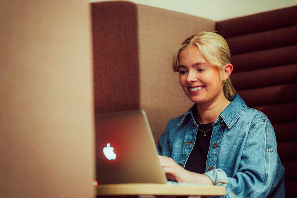 Smilende jente som studerer med en Mac foran seg.