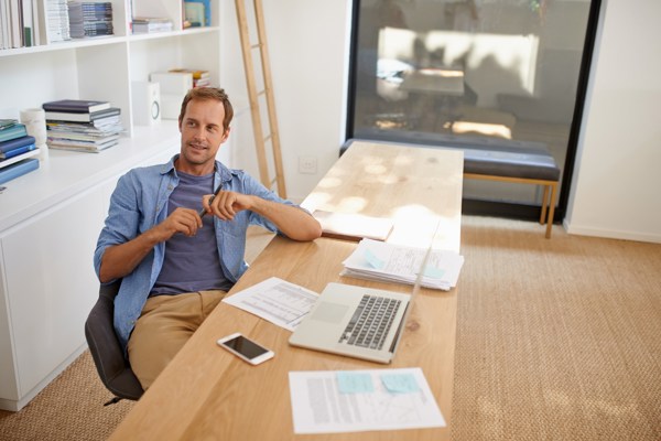 Mann i blå skjorte sitter ved pult med laptop og dokumenter.