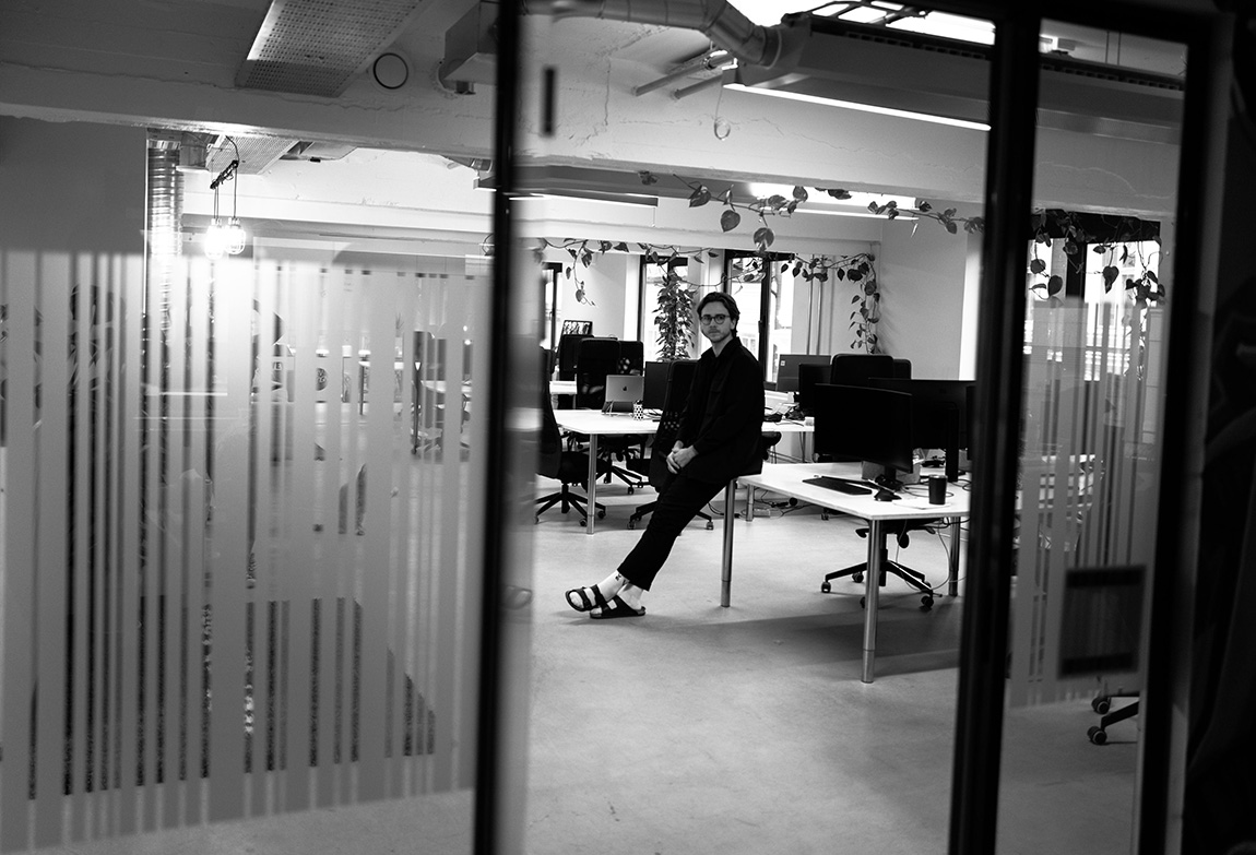 Fredrik Evjen Ekli lener seg mot en pult i et åpent kontorlandskap.