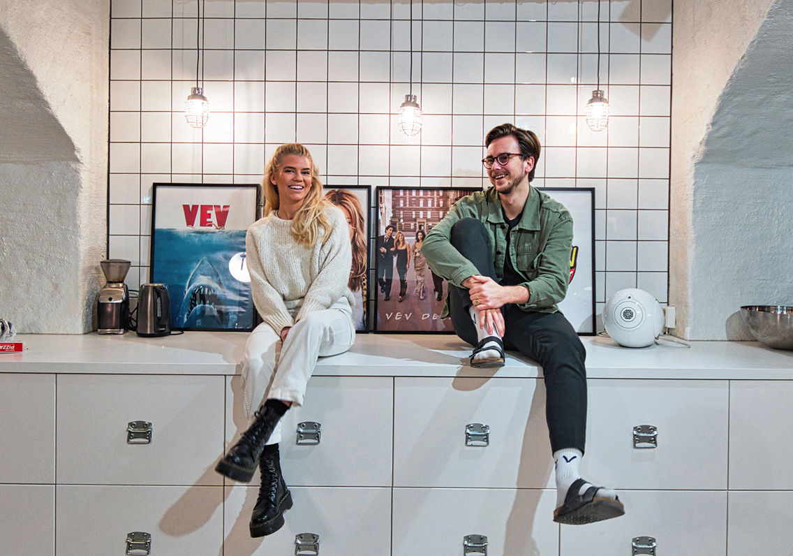 Tine Karlsen og Fredrik Evjen Ekli sitter på en kjøkkenbenk på kontoret og dingler med beina.