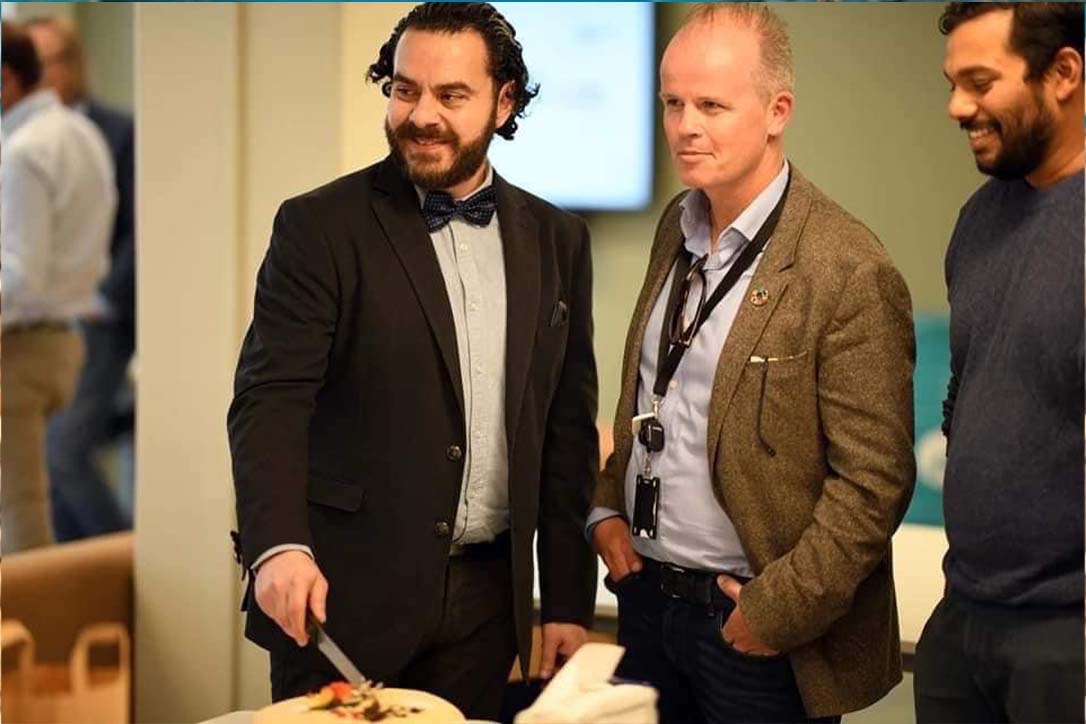 Professor Moutaz Haddara er fotografert sammen med IDEAS Lab-kollegaer Marius Langseth og Lester Lasrado Marius. Førstnevnte kutter opp en kake i anledning åpningen av IDEAS LAB mens alle smiler.