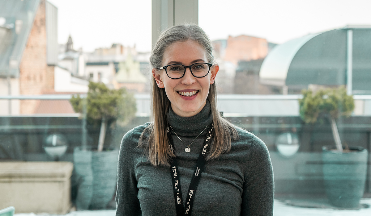 Nanna Nyquist står smilende mot kamera. Hun har på seg en grå turtleneck. Hun har sorte briller og rundt halsen har hun et smykke, og et nøkkelkort med logoen til Høyskolen Kristiania på. Bak henne kan man se lyse vinduer som viser deler av landskapet i Oslo sentrum.