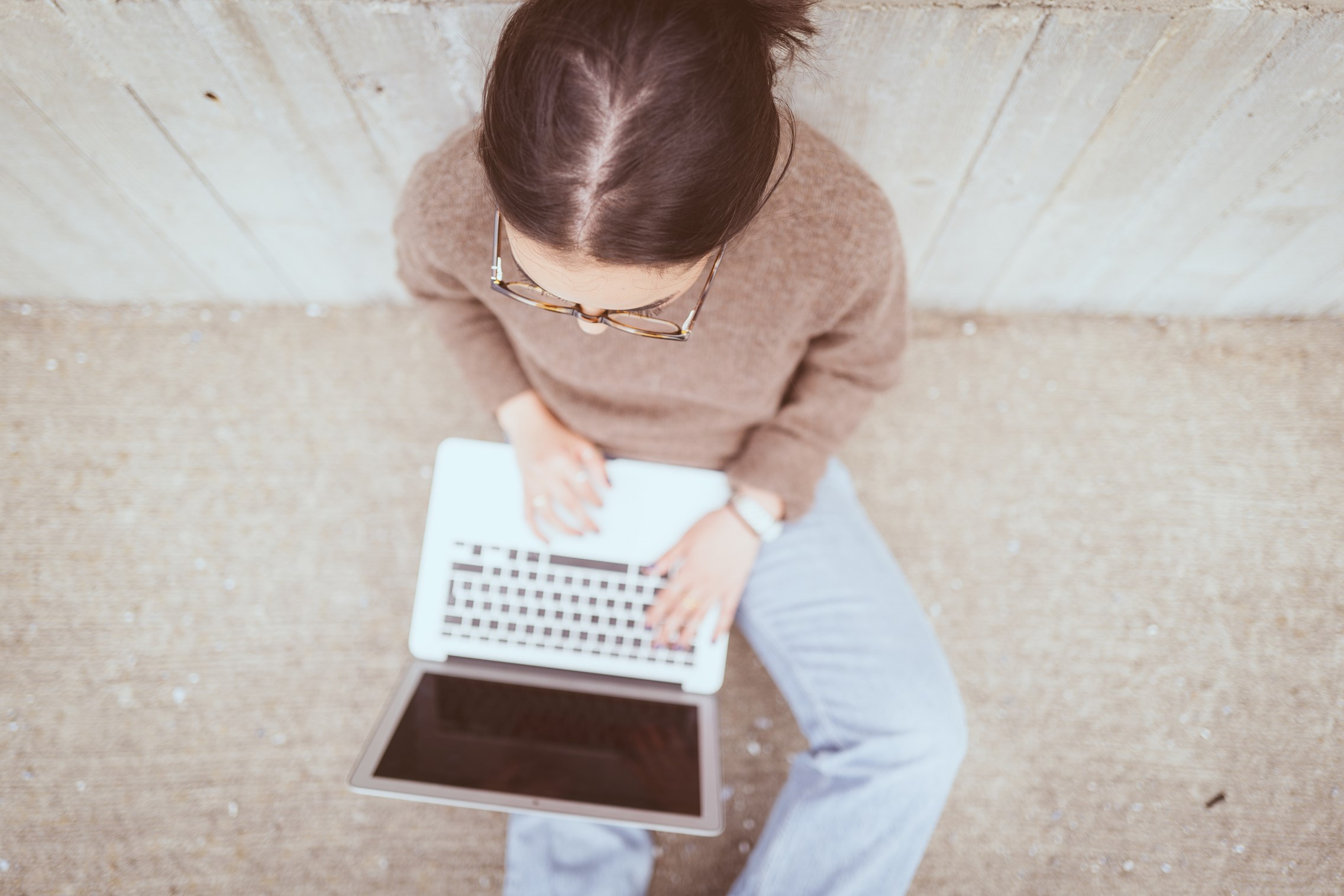 Kvinne, sett ovenfra og ned, skriver på en laptop mens hun sitter inntil en vegg.