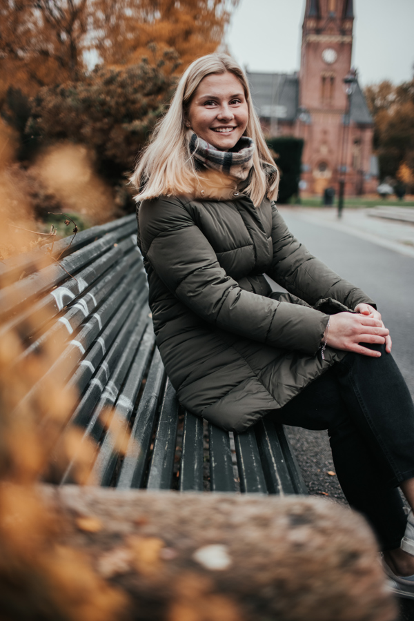 HR student Vilde på benk i Olaf Ryes plass. Jenta har på mørk høstjakke, rutete skjerf og har blondt hår.