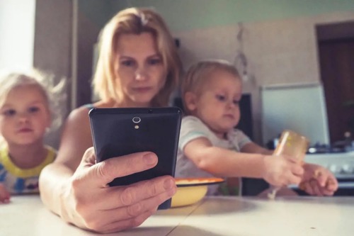 En dame sitter på telefonen mens hun har sine to barn på fanget som spiser