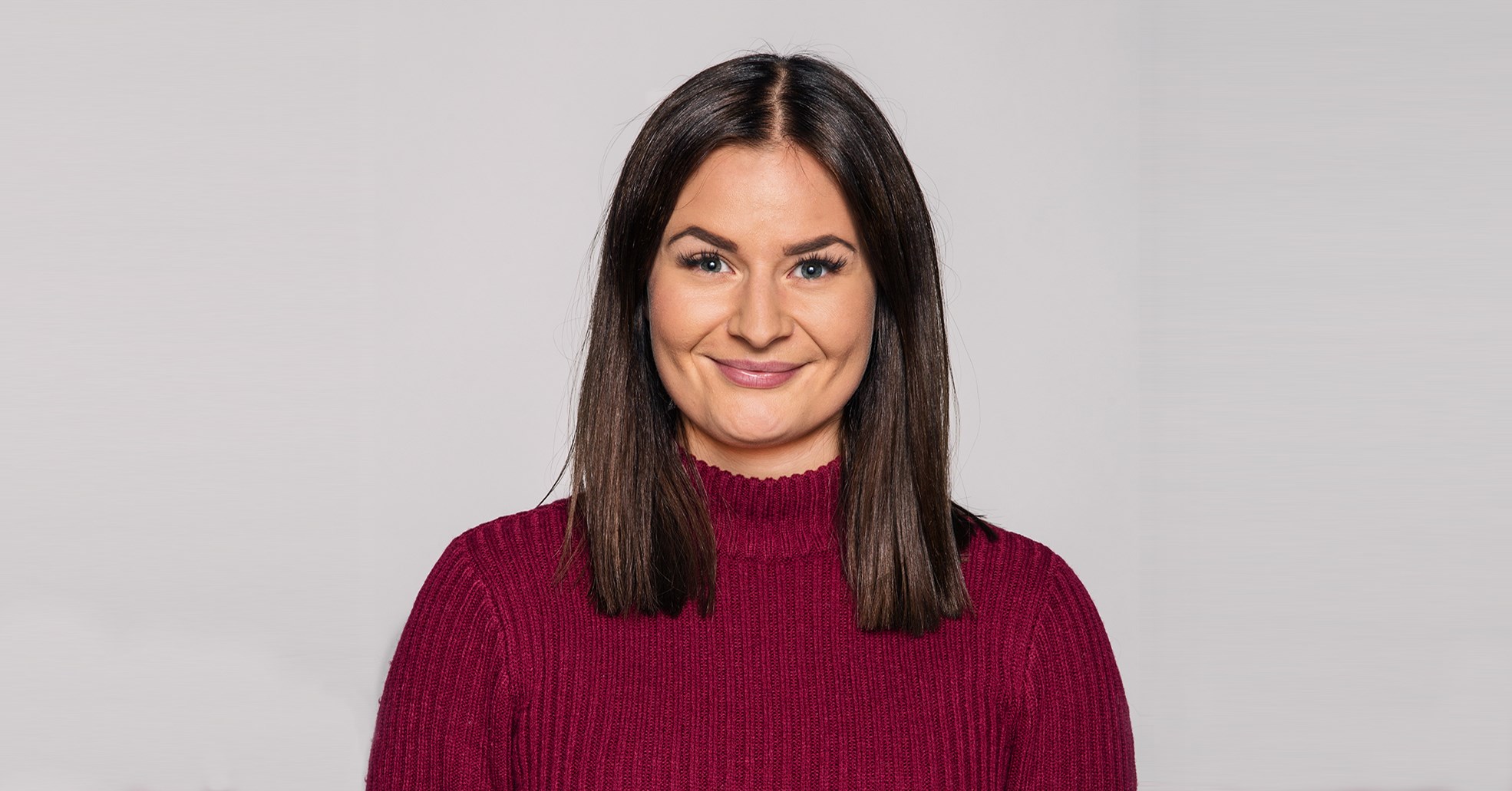 Foto av ung brunette i rød genser som smiler mot kamera.