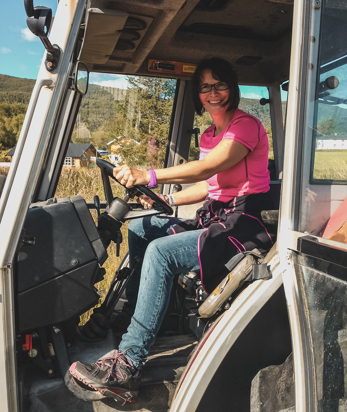 Solfrid Lind, administrerende direktør på Høyskolen Kristiania, sitter inne i en traktor. Hun har på seg en rosa t-skjorte og blå jeans. 