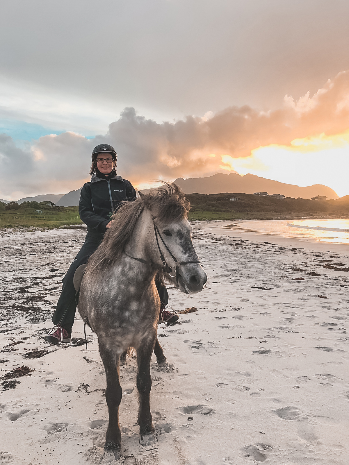 Solfrid Lind rir langs stranden i Loftoen. Bak henne kan man se en nydelig gul solnedgang. 