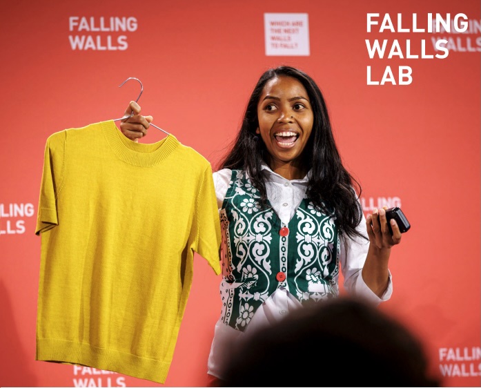 En kvinne som deltar på Falling Walls holder en gul genser mens hun forklarer idéen sin.