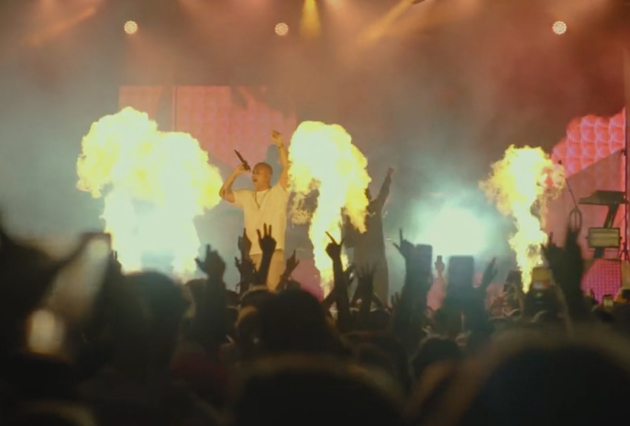 Bildelenke av artist på scene som danser bak pyroeffekter.