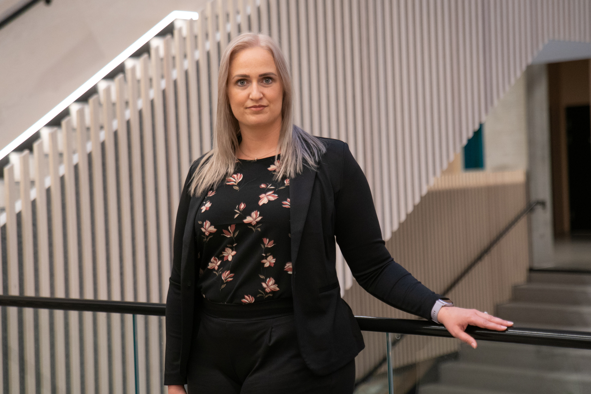 Malena står på Kristiania sitt campus og lener seg mot et rekkverk, med trapper i bakgrunnen.