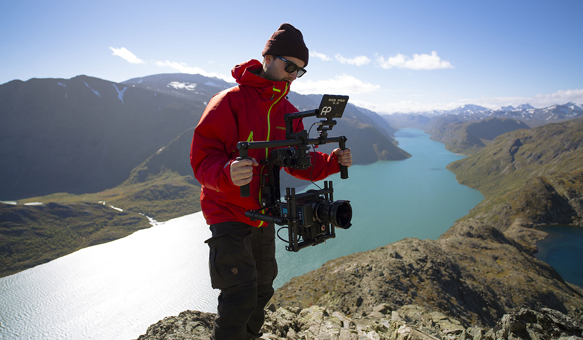 Ung mann med uteklær står på norsk fjell med kamera.