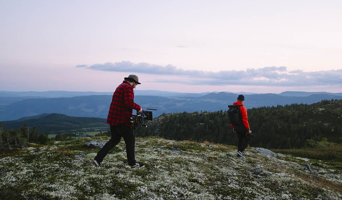 En mann filmer en annen som går over et naturlandskap