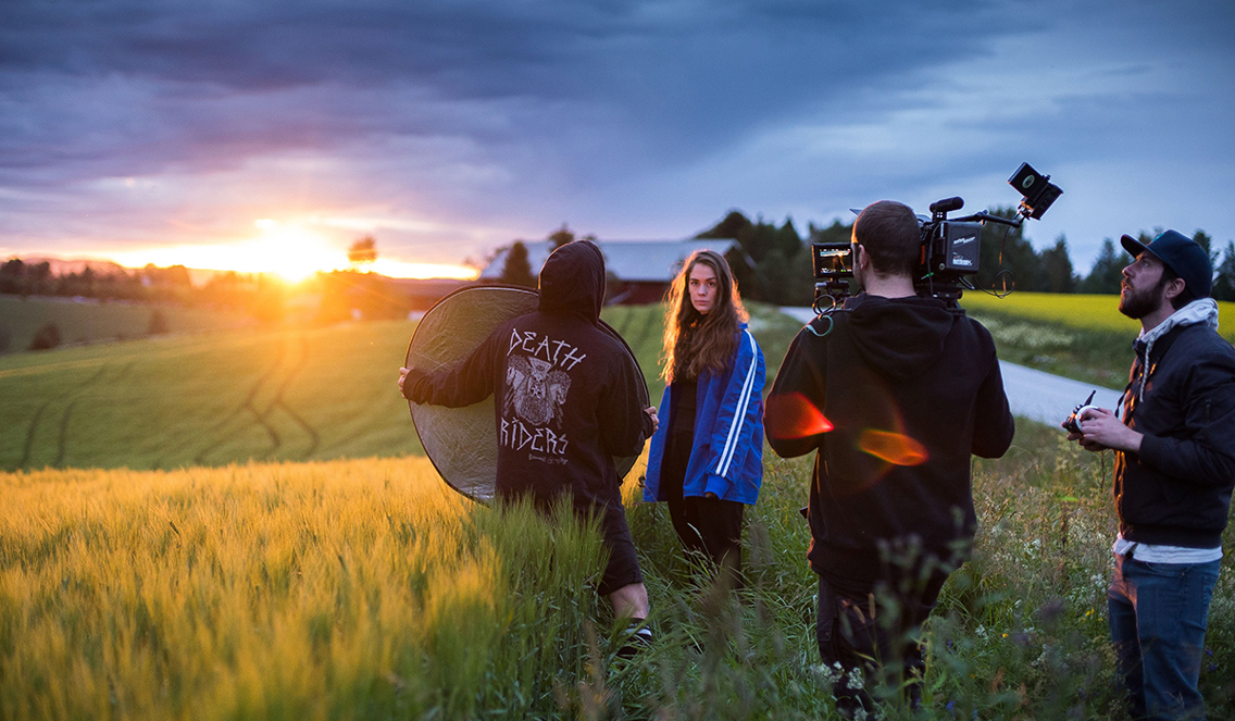 Ung dame på en eng i solnedgang med kamerassistenter