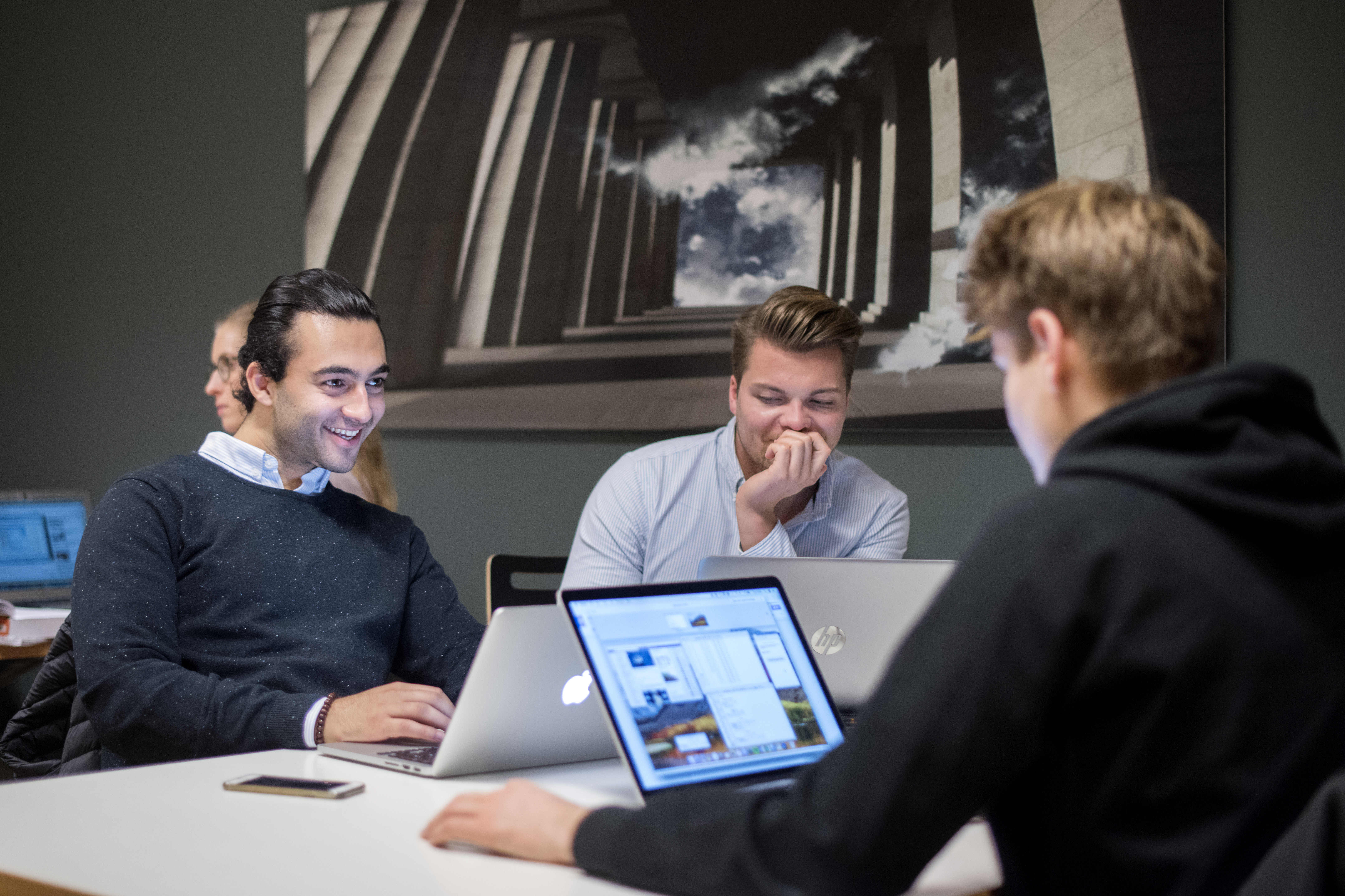 Foto av tre mannlige studenter rundt et bord, med hver sine PC-er.