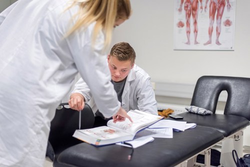 Foto av to legestudenter i frakker som leser i bok sammen,