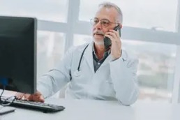 Doctor talking in the phone whilst looking at the computer screen