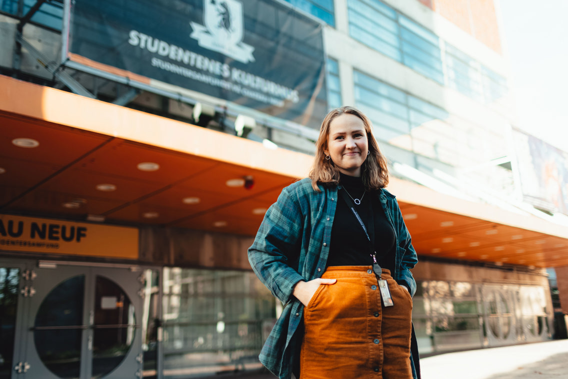 Ung kvinne i skjørt og flanellskjorte utenfor konserthus.