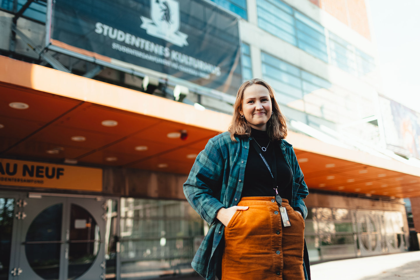 Ung kvinne i skjørt og flanellskjorte utenfor konserthus.