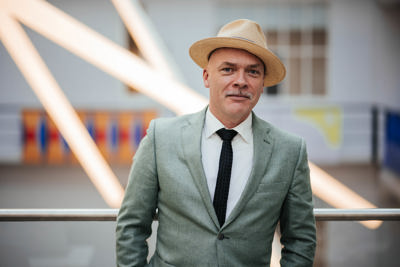 Mann i hvit skjorte og slips, grønn dressjakke og pen hatt.