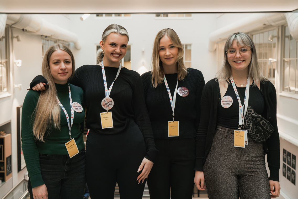 Foto av fire kvinnelige studenter med navneskilt og buttons i en gang.