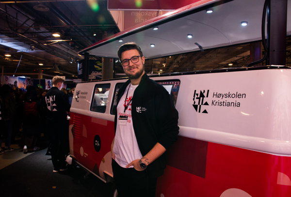 Foto av mannlig student foran en folkevognbuss med Kristiania-logo.
