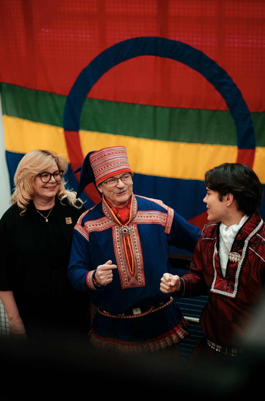 Trine sammen med artister Ánte Mikkel Gaup og tidligere student artist Vegard Bjørsmo foran det samiske flagget.