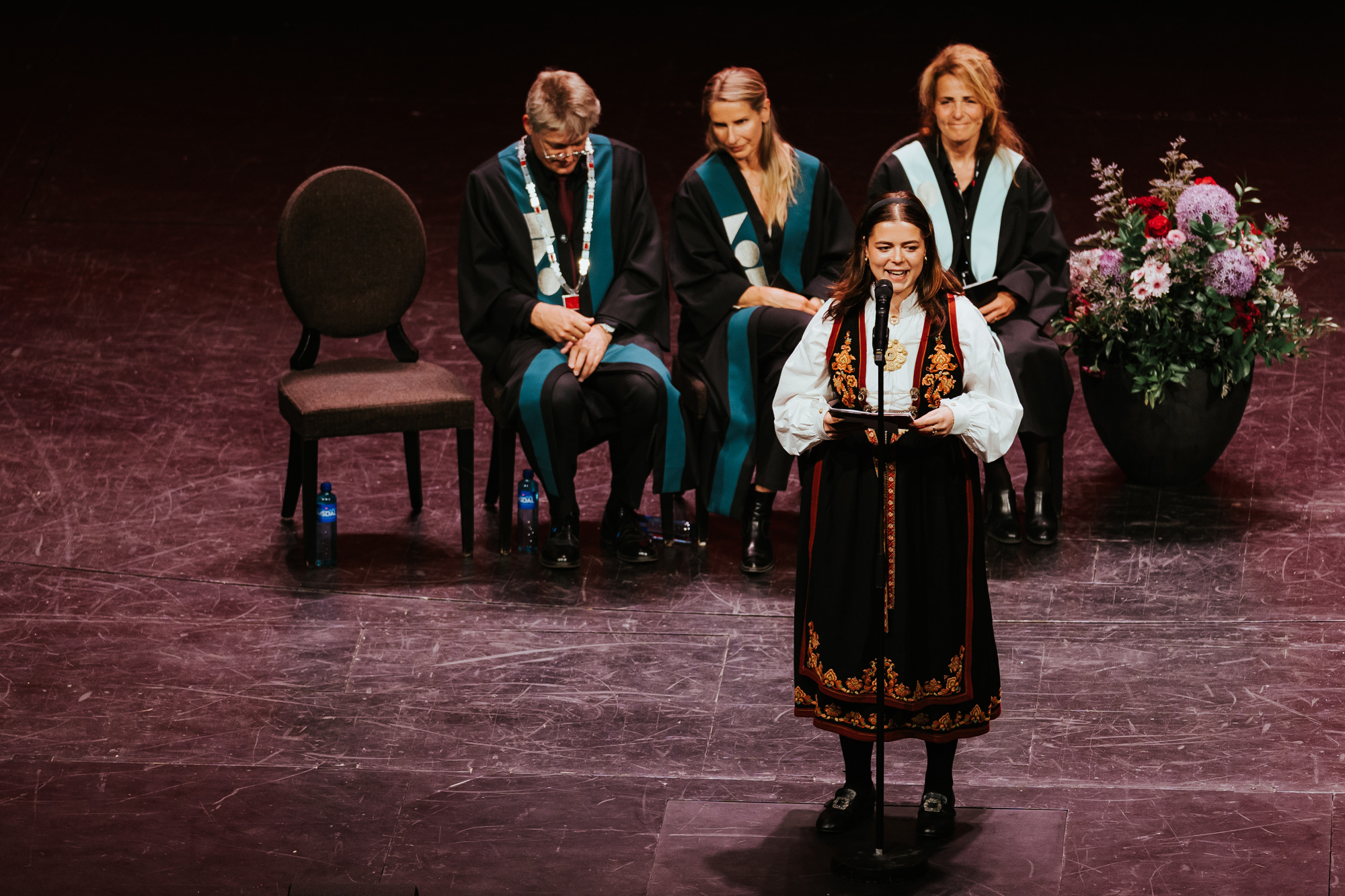 Kvinne kledd i bunad holder tale på scenen under avgangsseremoni ved Kristiania.